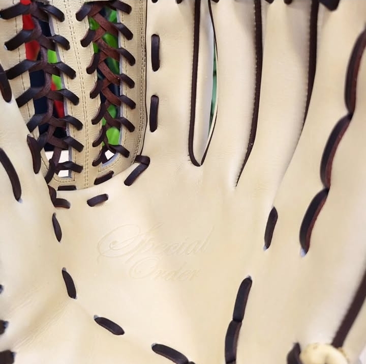Close-up of a beige baseball glove showing dark brown lacing and stitched panel seams.