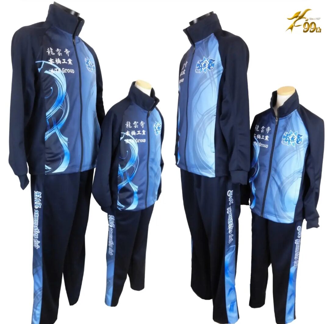 Group of blue and navy tracksuits in mixed sizes on mannequins, featuring swirling light-blue graphics and white branding text on the chest and legs.