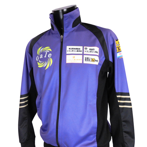 Purple and black zip-up athletic jacket on a mannequin, featuring sponsor logos on the chest and one sleeve.