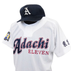 White baseball jersey with a navy cap perched on top; chest reads 'Adachi ELEVEN' in red/blue lettering, sleeve patches visible.